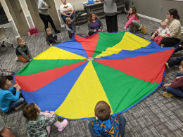 Children sitting around a colorful parachute.