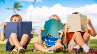 Three children holding books in front of their faces.