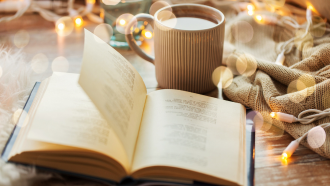 A book and a cup of coffee surrounded by twinkle lights.