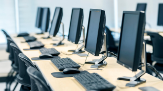 Computers and keyboards lined up on a desk.