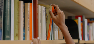 Hand selecting a book from a library shelf.